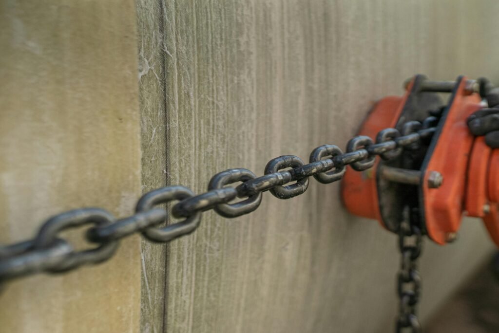 Home Detailed view of a metal chain connected to an orange pulley on a textured surface.