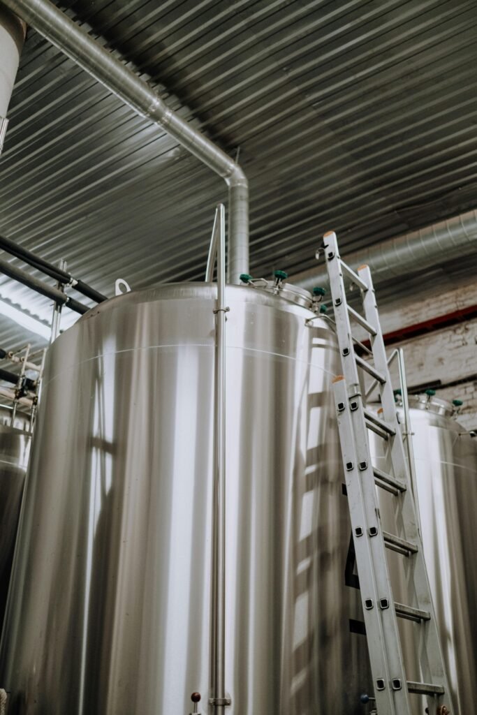 Vertical view of stainless steel fermenter tanks with a metal ladder in a brewery.